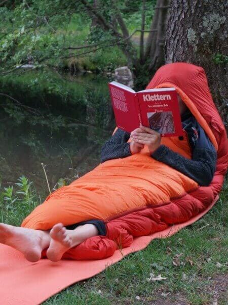 Person liest ein Kletterbuch in einem Schlafsack