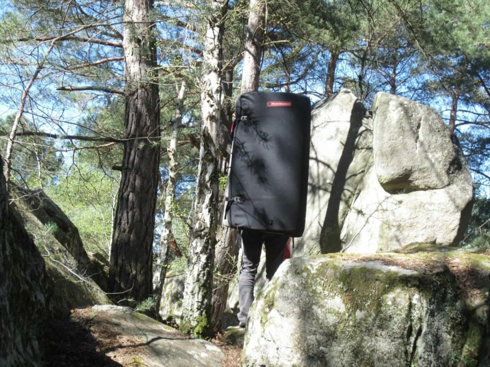 Person mit crashpad auf dem Rücken steht zwischen Felsen im Fontainebleau.