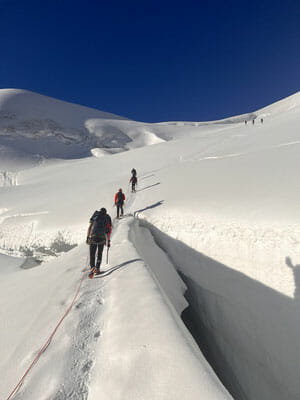 Die Seilschaft steigt beim Aufstieg auf den Piz Palü über Gletscherspalten hinweg.