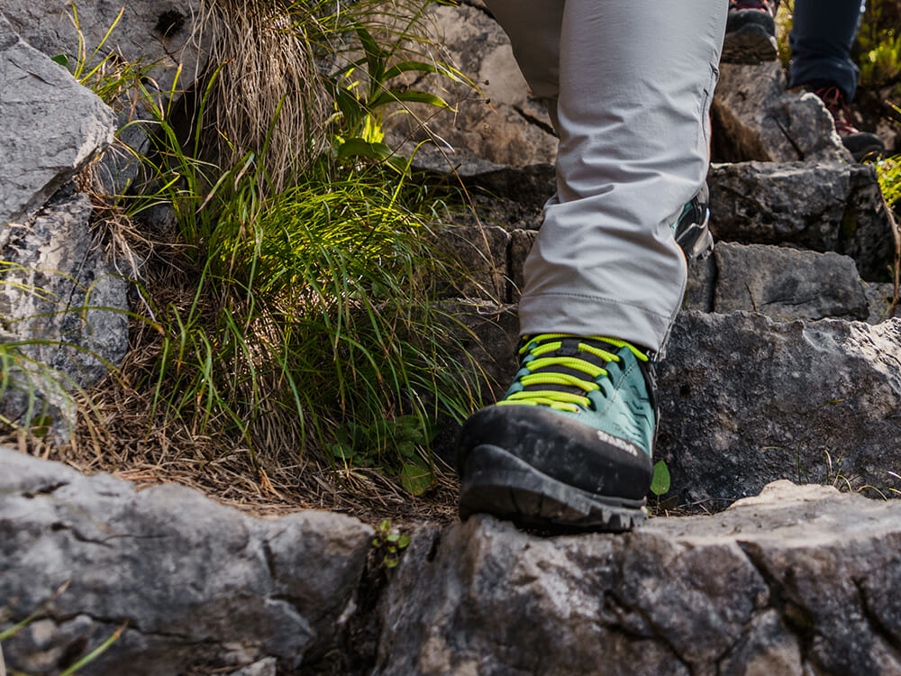 Bergfreundin beim Wandern. Besonders beim Abstieg auf felsigem Untergrund werden die Fußsohlen belastet. Hier können sich dämpfende Einlegesohlen lohnen.