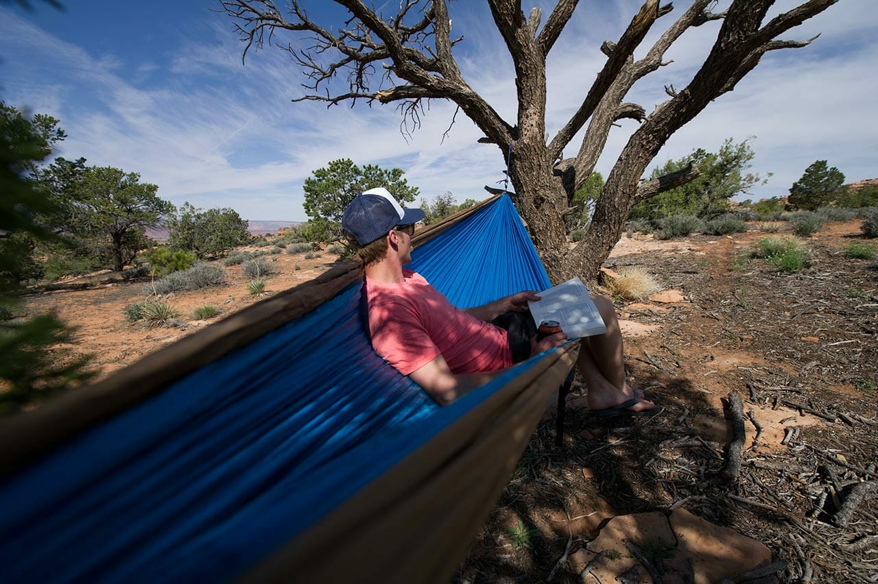 Mann liest Buch in einer Hängematte