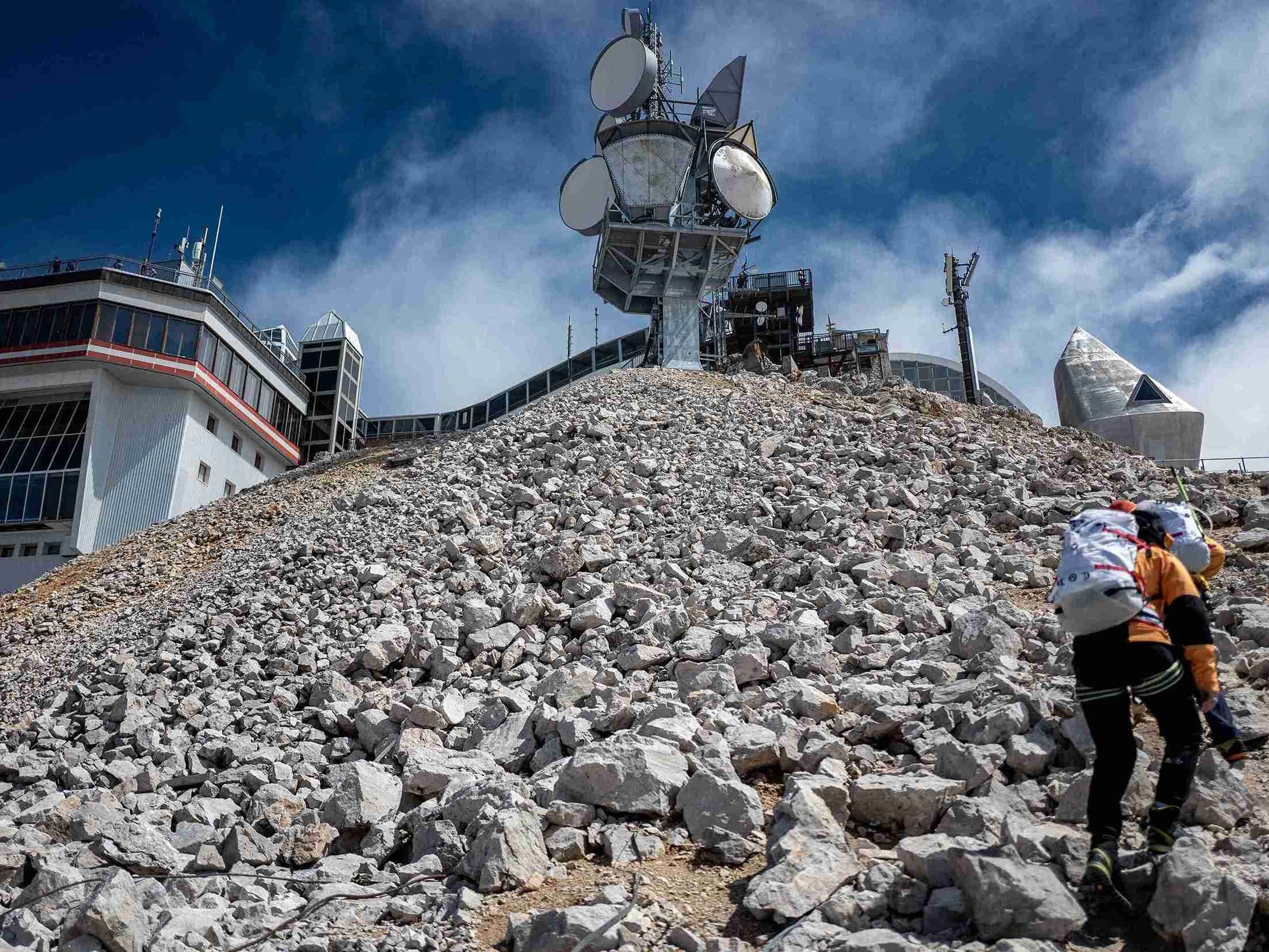 Ein Wanderer auf dem steinigen Gipfel mit Radar- und Sendeanlage im Hintergrund